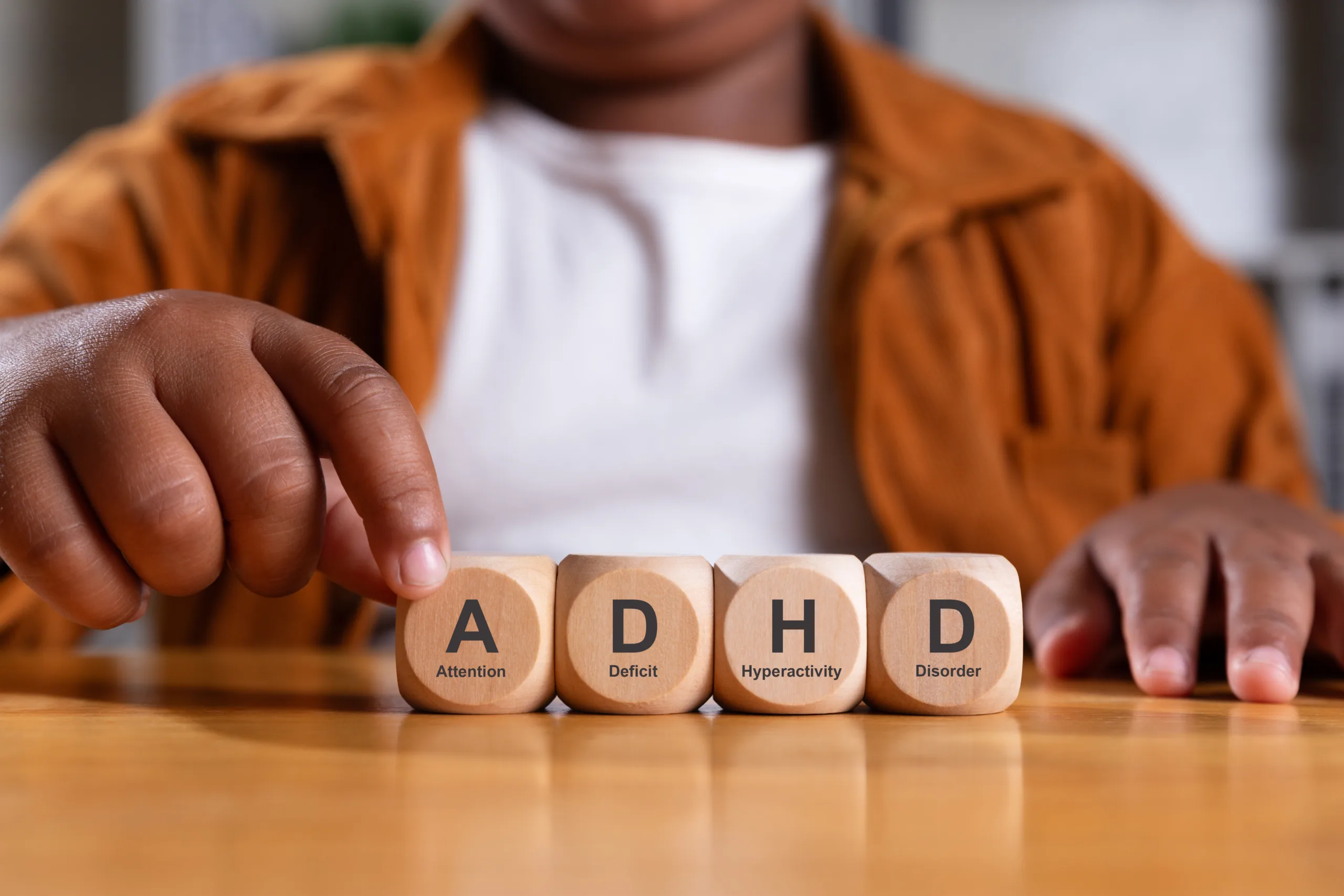 Hand of black boy puts wooden cube with ADHD,  Attention Deficit Hyperactivity Disorder on table.