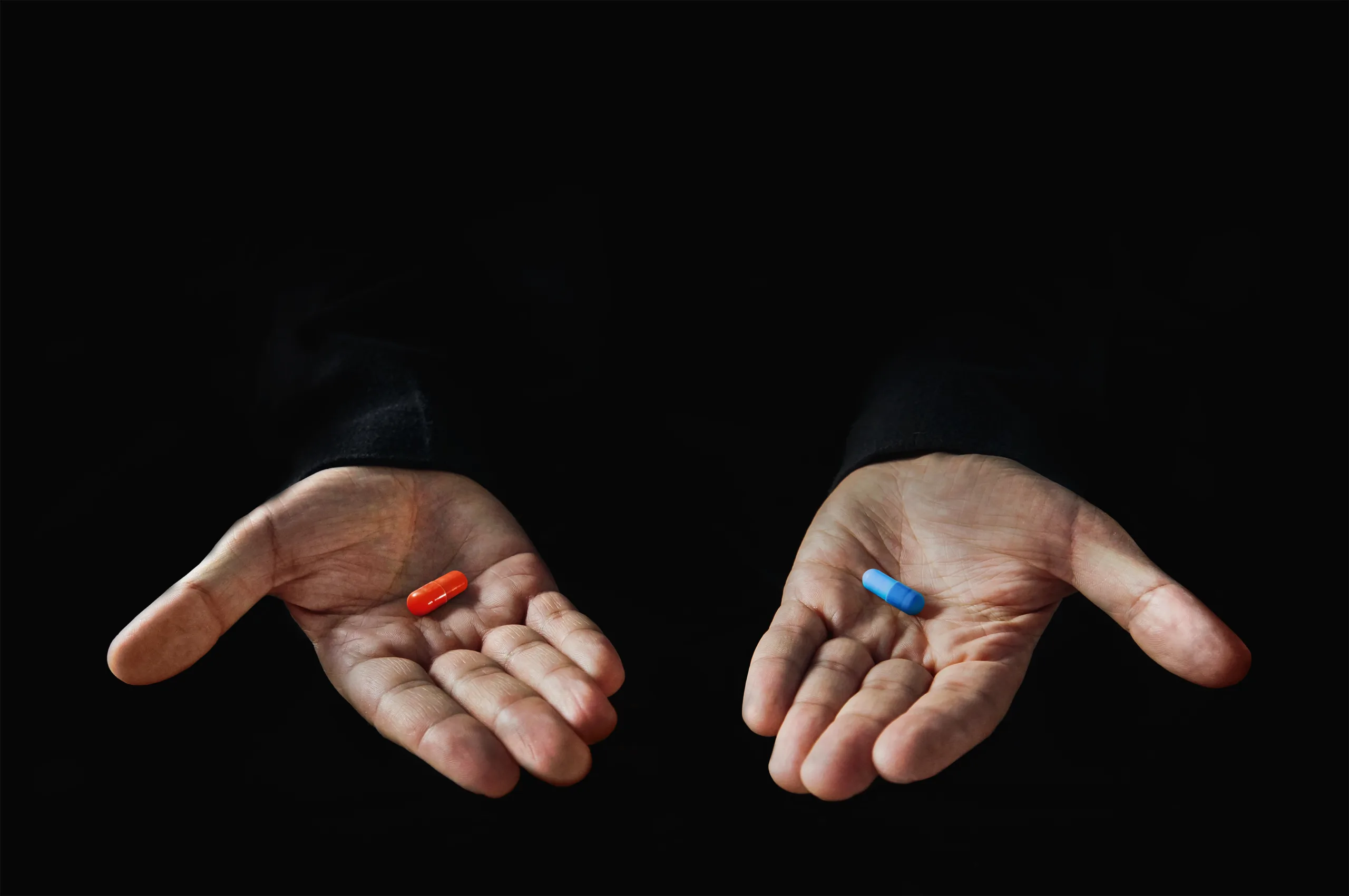 Red and blue pills on hand isolated on black background