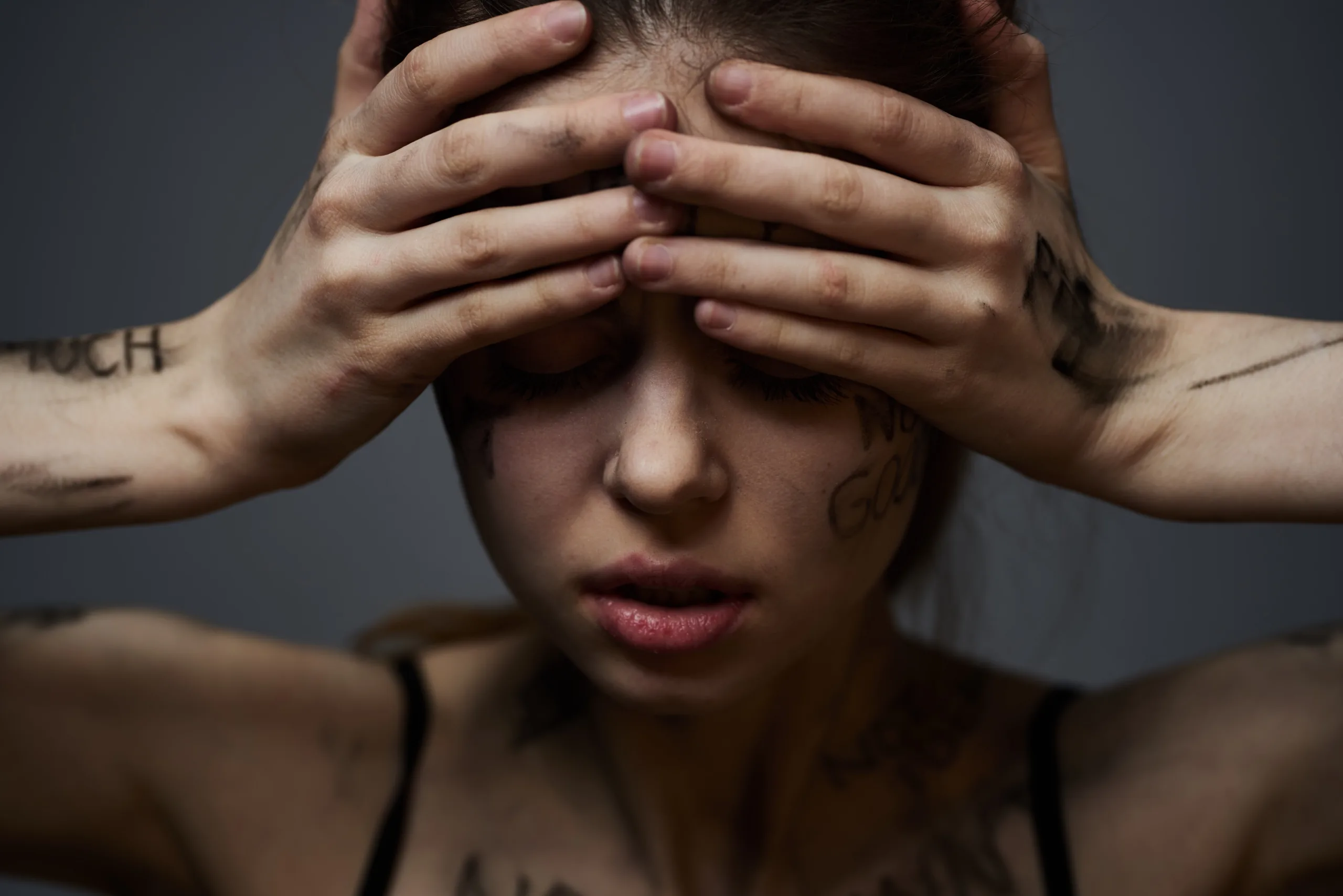 Frustrated woman with offensive inscriptions on her body and in a black T-shirt on a gray background portrait cropped view. High quality photo