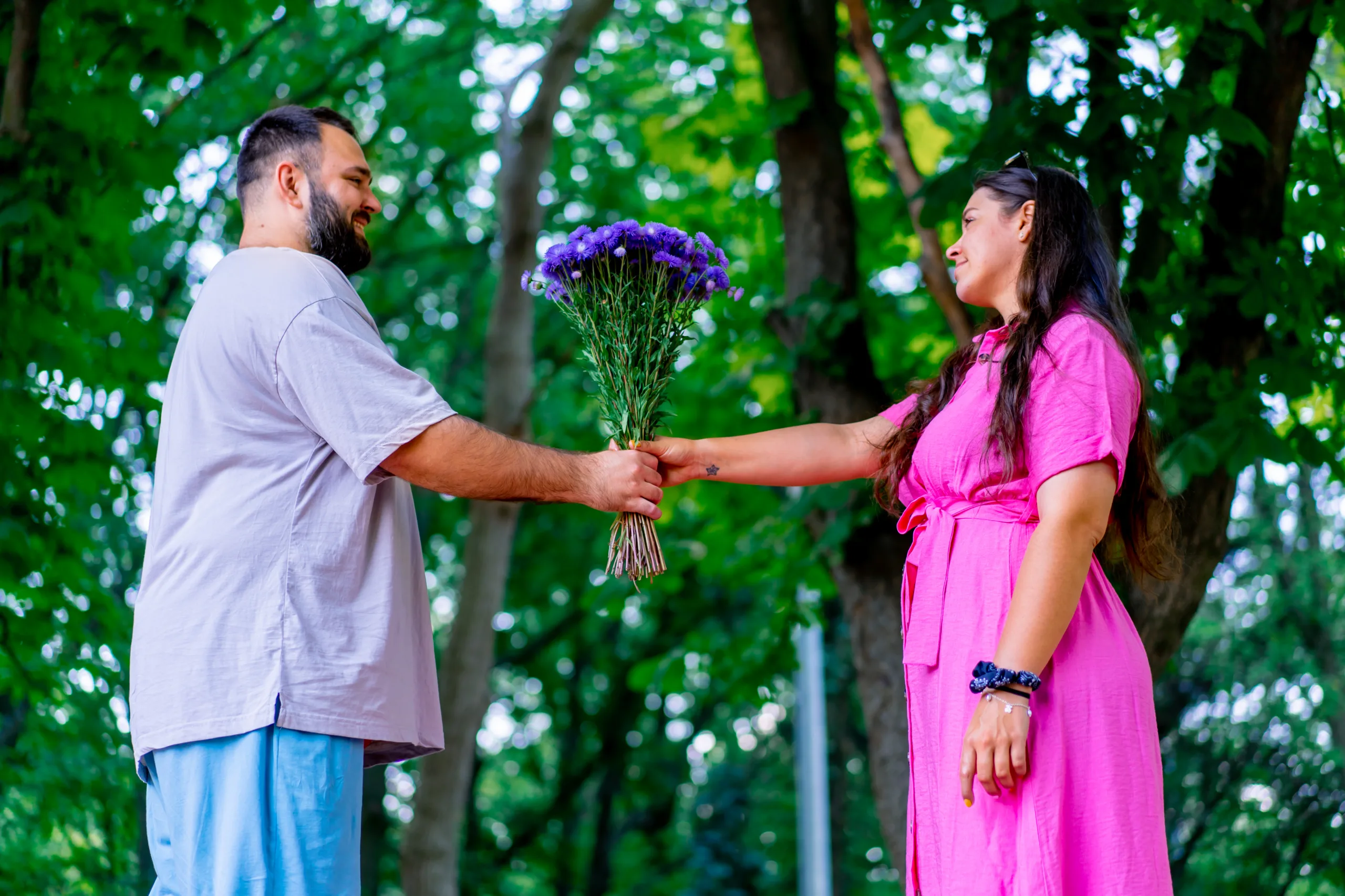 Young couple man gives bouquet of flowers to the girl in the park and she is happy about it